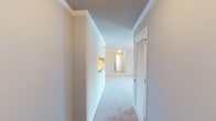Located at 1028 Kensington Manor Dr in Calera, Alabama, this single-floor home offers a well-organized layout designed for comfortable everyday living. The interior is finished with neutral tones throughout, creating a clean and cohesive aesthetic.

The hallway serves as the central connector of the home, featuring elegant crown molding, plush carpet underfoot, built-in cabinetry with a convenient shelf nook, and louvered closet doors that add a classic touch. The living area is generously sized with soft carpet, bright white walls, and access to the dining area, which is distinguished by crown molding and a gold-toned chandelier that adds a warm, inviting ambiance.

A bedroom with dual windows allows natural light to fill the space, complemented by a ceiling fan for added comfort. The kitchen is equipped with warm oak cabinetry, light countertops, wood-look flooring, and white appliances including a range, microwave, and refrigerator. A utility/laundry area with wire shelving and an electrical panel is conveniently accessible from the kitchen.

The bathrooms feature wood-tone vanity cabinetry with yellow countertops, large mirrors with vanity lighting, and tub/shower combinations with clean white surrounds. A spacious walk-in storage area with wire shelving and wood-look flooring provides excellent organizational capacity throughout the home.