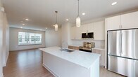 This well-designed three-bedroom, two-bathroom home spans three floors, offering a thoughtful layout with dedicated spaces for living, dining, and relaxing. The main living level features an open-concept kitchen and living area anchored by a striking quartz waterfall island with an integrated sink, complemented by pendant lighting and access to an outdoor balcony. The kitchen is outfitted with white shaker-style upper cabinets, warm wood-toned lower cabinets, stainless steel appliances including a French door refrigerator and electric range with microwave, and clean tile backsplash. Light hardwood-style flooring flows throughout the main level, enhancing the bright, airy ambiance created by recessed lighting and large windows. A pantry adds practical storage to the kitchen area. The bedrooms are carpeted for comfort, each featuring ample natural light through wide windows with views of the surrounding neighborhood. The spacious primary bedroom includes dedicated closet space. The bathrooms are finished in a clean, modern style with wood-toned vanities, full tub-shower combinations, and light flooring. Hallways and staircases connect each floor efficiently, while additional closets provide generous storage. The overall aesthetic is clean, contemporary, and move-in ready.