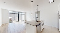 This well-appointed 2-bedroom, 2-bathroom unit in Baltimore, MD offers a thoughtfully designed open-concept layout across a single floor. The living area is bathed in natural light thanks to expansive floor-to-ceiling sliding glass doors fitted with vertical blinds, opening to outdoor views of the surrounding cityscape and providing a bright, airy atmosphere with light hardwood flooring throughout.

The kitchen is a standout feature, centered around a generous granite-topped island with an undermount sink and matte black faucet, complemented by pendant lighting overhead. White shaker cabinetry with black hardware lines the walls, paired with a herringbone tile backsplash and a full suite of stainless steel appliances, including a refrigerator, range, and over-the-range microwave.

Both bedrooms are carpeted and well-proportioned, each featuring large windows with horizontal blinds that frame outdoor views and allow ample natural light. The primary bedroom offers a comfortable footprint with dedicated closet space.

The two bathrooms share a consistent, clean aesthetic with wood-plank-style tile flooring, white subway tile tub surrounds, white vanity cabinetry, and matte black fixtures throughout. The overall design is modern and cohesive, combining neutral tones with contemporary finishes to create a polished, move-in-ready living space.