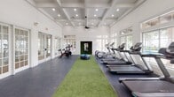 Located at 1802 Ennis Joslin Rd in Corpus Christi, TX, this single-floor fitness center is designed to support a full range of training disciplines in a clean, modern environment. The facility is characterized by soaring coffered ceilings, recessed lighting, and large windows that invite abundant natural light and outdoor views of the surrounding palm-lined landscape and pool area.

The main workout floor is divided into distinct functional zones. The cardio section is outfitted with multiple treadmills, elliptical machines, stair climbers, stationary bikes, and a rowing machine, all arranged along windowed walls to provide an open, airy feel during exercise. A central artificial turf lane runs the length of the facility, serving as a dedicated functional training corridor equipped with battle ropes, plyo boxes, and a tire for high-intensity workouts.

The strength training area features a power rack, cable machines, a punching bag, a weight bench, medicine balls, and a variety of accessories neatly organized on wall-mounted storage racks. Motivational signage adorns the walls, reinforcing an energizing atmosphere. Ceiling fans throughout ensure comfortable airflow.

A storage unit with built-in cabinetry and cubbies provides organized equipment storage, and French doors connect areas seamlessly. Durable rubber and epoxy flooring throughout ensures safety and longevity, making this fitness center a comprehensive and well-appointed training destination.