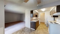 Located at 8719 N Hill N Dale St in Spokane, WA, this single-floor unit offers a functional and straightforward layout designed for comfortable everyday living. The kitchen is positioned at the heart of the space, featuring dark wood cabinetry — both upper and lower — light countertops, a double-basin sink, a white electric range with overhead ventilation, and a white refrigerator. Durable tile-style flooring runs throughout the kitchen and entry areas, providing easy maintenance underfoot. The kitchen opens directly to a generously sized living area finished with wall-to-wall carpeting and a ceiling fan overhead, creating a seamless flow between cooking and relaxing spaces. A sliding glass door in the living area fills the room with natural light and provides access to an outdoor balcony with views of surrounding greenery. The bedrooms are carpeted and well-proportioned, each featuring ceiling fans and closet storage with dark wood doors. Baseboard heating units are present in the bedrooms, ensuring year-round comfort. Textured ceilings are consistent throughout, and neutral wall tones provide a clean, move-in-ready canvas. The overall layout is practical and cohesive, making efficient use of its single-floor footprint.
