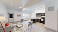 This single-floor residence is designed with a clean, contemporary aesthetic that emphasizes open space and functional living. The heart of the unit is a generously proportioned open-concept area where the living room and kitchen flow seamlessly into one another. Elevated ceilings with exposed beam detailing add architectural interest and amplify the sense of volume throughout the main living space. Light wood-tone flooring runs consistently across the area, contributing to a cohesive and airy feel.

The living area comfortably accommodates seating arrangements and benefits from abundant natural light streaming through a large window that offers views of the surrounding neighborhood. A dedicated dining nook sits adjacent to the kitchen, defined by a countertop overhang ideal for casual seating.

The kitchen is outfitted with dark espresso cabinetry paired with light granite-style countertops, a double-basin sink, black appliances including an electric range and dishwasher, and ample upper and lower cabinet storage.

The bedrooms are well-proportioned, featuring neutral carpeting or hard flooring, bright windows with outdoor views, and a calm, restful atmosphere. The bathroom presents a clean, modern finish with tile flooring, a dark vanity with integrated sink, and crisp white walls throughout.