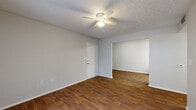 This single-floor residence offers a thoughtfully arranged layout with a clean, neutral aesthetic throughout. The main living areas feature warm, rich hardwood-style flooring and textured ceilings, with ceiling fans providing both function and a sense of comfort. The living room is bright and open, offering direct access to an outdoor area through sliding glass doors dressed with vertical blinds, allowing generous natural light to fill the space.

The galley-style kitchen is efficiently designed with light wood cabinetry lining both sides, white appliances including a gas range, microwave, refrigerator, and dishwasher, along with ample counter space and a double-basin sink — making it well-suited for everyday cooking.

The bedrooms are carpeted for comfort and each feature ceiling fans and built-in closets with shelving, offering practical storage. The rooms are bathed in soft, neutral tones that create a calm and restful atmosphere. One bedroom benefits from a window with views of surrounding greenery.

The bathroom is neatly appointed with a wood-framed vanity mirror, a single-sink vanity with a speckled countertop, and a full tub-shower combination. A dedicated in-unit laundry area accommodates a full-sized washer and dryer side by side, adding everyday convenience to this well-rounded residence.