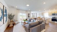 This two-story home is designed with a clean, contemporary aesthetic that emphasizes natural light and an open, airy feel throughout. The main level centers on a seamlessly connected living, dining, and kitchen area finished with warm hardwood-style flooring. The living room offers generous seating space and is anchored by large sliding glass doors that open to an outdoor patio, flooding the room with natural light and providing views of the surrounding landscape. Bold artwork adds a striking accent to the neutral walls.

The kitchen features light wood cabinetry, a white quartz island with bar seating, stainless steel appliances, and recessed lighting. Adjacent to it, the dining area is framed by multiple windows with open countryside views, creating an inviting atmosphere for gatherings. A compact half bath with hardwood flooring completes the main level.

Upstairs, a bright landing with windows serves as a versatile flex space. The primary bathroom showcases a dual-sink vanity with white quartz countertops, wood-look flooring, decorative wallpaper, and access to a walk-in closet. Additional bedrooms are carpeted and offer distinct character, including one with charming floral wall decor.