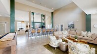 Located at 1104 Diamondback Dr in Sneads Ferry, NC, the Comet Sneads Ferry clubhouse is a thoughtfully designed single-floor community space that blends coastal charm with modern sophistication. The interior is anchored by soaring ceilings and bold teal-green architectural columns that create striking visual continuity throughout the open floor plan. Polished concrete floors reflect abundant natural light, lending an airy, upscale ambiance to every area.

The living room area offers generous seating with plush neutral sofas and botanical-print accent chairs arranged around a central coffee table, complemented by curated coastal artwork. Adjacent to this is a stylish bar featuring a geometric-tiled facade, leather barstools, and built-in teal shelving — an ideal gathering spot. A game area with a pool table and shuffleboard adds a recreational dimension to the space.

The dining room is an intimate, private area accessed via a sliding barn door, furnished with natural wood cane chairs, a round wood-framed mirror, and soft carpet underfoot. A dedicated office with French doors, a woven pendant light, and views of the surrounding greenery provides a functional workspace.

Outside, a covered patio with comfortable lounge seating overlooks a resort-style pool, completing this well-appointed community destination.