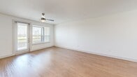 This three-story home in Dallas, Texas offers a well-organized layout across three distinct floors. The ground level houses an attached garage with an automatic opener and direct interior access, along with a tidy entry hallway with wood-look flooring and carpeted stairs leading to the upper levels. The main living floor features an open-concept kitchen and living area. The kitchen is appointed with light wood cabinetry extending to the ceiling, white quartz countertops, a subway tile backsplash, stainless steel appliances including a refrigerator with ice maker and a built-in microwave, and a central island with a sink and pendant lighting overhead. Wood-look flooring flows throughout this level, and a ceiling fan with a window provides natural light to the living area. The upper floor is dedicated to three bedrooms, each finished with plush carpet and ceiling fans. Bedrooms are well-lit by large windows with neighborhood views, and each includes closet space, with some featuring built-in shelving and double hanging rods. The home includes four bathrooms, each designed with light wood vanities, white quartz countertops, large mirrors, and wood-look flooring. Select bathrooms feature tile-surround showers, adding a refined touch throughout.