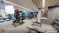 Located at 910 Willow Dr in Chapel Hill, NC, this professionally designed fitness center offers a comprehensive exercise environment across a generously sized single floor. The space combines contemporary aesthetics with high-functionality, featuring a neutral carpet floor, concrete-finish columns, and a clean white ceiling adorned with sleek linear LED lighting that ensures bright, even illumination throughout.

The strength training zone is well-appointed with a variety of cable machines, weight benches, squat racks, and free weight stations, complemented by medicine balls, resistance bands, and stability balls neatly organized on dedicated racks. Dark navy accent walls and large mirrors amplify the sense of depth and space while allowing users to monitor their form.

The cardio section is positioned along a floor-to-ceiling glass window wall that floods the area with natural light and provides views of the outdoors. Treadmills, stationary bikes, rowing machines, Peloton bikes, and elliptical trainers are arranged to maximize both space and access to the natural light.

Decorative wood-slat ceiling details in one section add a warm, upscale touch to the otherwise modern industrial design. The overall ambiance is energetic yet polished, creating an inviting, motivating environment suited for a wide range of fitness activities.