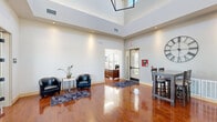 Located at 1719 Moon Meadows Dr in Rapid City, South Dakota, this single-story community facility offers a thoughtfully designed layout across a generous footprint. The space is organized into four distinct areas, each serving a specific function while contributing to an overall cohesive and polished environment.

The entry lobby immediately impresses with soaring double-height ceilings, gleaming hardwood floors, and abundant recessed lighting. A seating area with leather accent chairs provides a welcoming reception space, while a front desk area is visible through an adjacent doorway. Large windows and a glass entry door invite natural light throughout.

The lounge area features dramatic floor-to-ceiling windows that flood the room with daylight and offer outdoor views. A sleek linear fireplace with mosaic tile detailing and a wall-mounted television anchor the space, complemented by leather sofas and a central coffee table, creating a refined gathering area.

The kitchen is equipped with rich dark wood cabinetry, granite countertops, stainless steel appliances, a large island with bar seating, pendant lighting, and a decorative tile backsplash — ideal for community events and gatherings.

The fitness center is spacious and well-lit, featuring treadmills, ellipticals, stationary bikes, a power rack with free weights, and wall-mounted monitors. Natural light pours in through large windows. The facility also includes fully tiled restrooms with private shower stalls, granite vanities, and upscale tile work throughout.