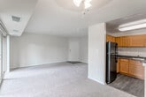 This single-floor residence offers a well-organized layout with distinct living, kitchen, bedroom, and bathroom areas. The spacious living room is finished with neutral-toned carpet and neutral wall colors, creating a bright, open atmosphere. Large sliding glass doors lead to a private balcony with black metal railing and tree-lined views beyond, allowing natural light to fill the space. A second large window in one of the bedrooms further enhances the connection to the outdoors with green tree views.

The kitchen is separated from the living area by a partial wall and features warm oak cabinetry extending to the ceiling, dark granite-style countertops, and durable wood-look flooring. Black appliances, including a refrigerator, gas range, and dishwasher, complement the cabinetry. A pantry closet provides additional storage. The bathroom is finished with classic white subway tile surrounding the tub and shower, a framed mirror, an oak vanity with a white countertop, and tile flooring. The bedroom is generously sized with carpet flooring and includes closet access, completing this functional and cohesive layout.