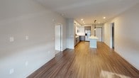 This single-floor unit presents a clean, modern aesthetic throughout its well-appointed layout. The kitchen is a standout feature, showcasing two-tone cabinetry with sleek gray lower cabinets and white upper cabinets, complemented by a textured tile backsplash. Stainless steel appliances — including a gas range, microwave, dishwasher, and refrigerator — pair with white quartz countertops and a central island with pendant lighting overhead. Wood-look vinyl flooring extends through the kitchen and into the open living area, which is bright and generously proportioned with recessed lighting and access to the outdoors. The bedrooms are finished with plush carpet and feature sliding windows offering views of surrounding greenery, with one bedroom including a ceiling fan. Two bathrooms serve the unit: one features a gray vanity with a large mirror, white countertop, and a soaking tub with built-in shelving, while the second includes a glass-enclosed shower, a matching gray vanity, and wood-look flooring. A dedicated in-unit laundry closet houses a stacked washer and dryer. The overall design is cohesive, with neutral tones and contemporary finishes throughout.