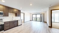 This thoughtfully designed 2-bedroom, 2-bathroom residence features a contemporary open-concept layout that seamlessly connects the kitchen and living areas. The kitchen is appointed with dark espresso cabinetry, white quartz countertops, a subway tile backsplash, and a full suite of stainless steel appliances including a refrigerator, range, microwave, and dishwasher. Light wood-tone flooring runs throughout the main living areas, enhancing the bright, airy ambiance created by recessed lighting overhead. The living room opens directly onto a private balcony through floor-to-ceiling sliding glass doors, bringing in natural light and outdoor views. Both bedrooms feature plush carpeting and dedicated closets, with the primary bedroom benefiting from a spacious walk-in closet with wire shelving systems. The two bathrooms are finished with marble-look tile flooring and dark vanity cabinetry with white countertops; one bathroom includes a tiled tub-shower combination with brushed nickel fixtures. A dedicated in-unit laundry room with a full-size washer and dryer adds everyday convenience. The clean, neutral palette and modern finishes throughout create a cohesive, move-in-ready living environment.
