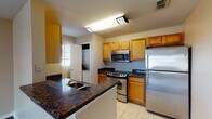 This single-floor residence offers a well-organized layout that balances functionality and comfort throughout its living spaces. The open-concept design connects the kitchen and living area seamlessly, creating a cohesive and practical flow.

The kitchen is equipped with stainless steel appliances, including a refrigerator, electric range, and over-the-range microwave. Warm honey-toned cabinetry provides ample storage, while dark granite countertops add visual contrast. A peninsula with a built-in sink and matching dark granite surface doubles as a casual dining or prep area. Light ceramic tile flooring and overhead lighting complete the space. A laundry area with stacked or side-by-side units is accessible directly from the kitchen.

The living area features rich dark hardwood-style flooring, neutral beige walls, and multiple windows fitted with blinds, allowing natural light to fill the room. A ceiling fan with integrated lighting adds comfort and practicality.

The bedrooms are carpeted, with neutral tones and natural light from window, and include closets with louvered doors. Both bathrooms feature tile flooring, granite-topped vanities with wood cabinetry, and large mirrors. One bathroom includes a shower-tub combination with white tile surround, while the other offers a separate shower area.