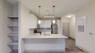 The Dogwood is a single-story, three-bedroom, two-bathroom residence thoughtfully designed to maximize both function and comfort. The open-concept layout creates a seamless flow between the main living areas, making the space feel expansive and connected.

The kitchen serves as a central feature of the home, showcasing white shaker-style cabinetry that extends to the upper walls for generous storage capacity. Stainless steel appliances, including a refrigerator, microwave, and range, provide a sleek, modern aesthetic. A large peninsula with a granite-style countertop and an integrated sink extends into the living area, offering additional prep space and casual seating. Pendant lighting hangs above the peninsula, complementing the recessed and track lighting that illuminates the kitchen.

The flooring throughout the main living area features wood-style planking that adds warmth and durability. Neutral wall tones contribute to a clean, versatile palette that suits a variety of décor styles. The residence also includes a dedicated entry door, providing a clear separation between interior and exterior spaces. With three bedrooms and two full bathrooms, the Dogwood offers ample space for comfortable everyday living.