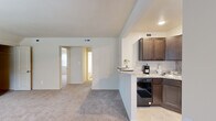 This renovated single-floor residence at 5606 Burtis Ave in Baltimore, Maryland offers a thoughtfully updated interior with a clean, neutral palette throughout. The open-concept layout connects the living area to the kitchen via a peninsula counter, creating a practical and sociable flow between spaces. The kitchen is a standout feature, outfitted with rich dark-stained shaker-style cabinetry, granite countertops with a complementary tile backsplash, and a full suite of Whirlpool appliances including a refrigerator, range with overhead microwave, and dishwasher. Soft carpeting extends throughout the living areas and bedrooms, contributing to a warm and comfortable ambiance. The primary bedroom is generously proportioned, offering a closet and direct access to an adjoining room, providing flexible use of space. Additional bedrooms are bright and airy, each featuring ceiling fans and windows that invite natural light and outdoor views of the surrounding greenery. The bathroom has been cleanly renovated with a white vanity, tiled tub-shower combination, and a large wall mirror. Natural light filters through multiple windows across the home, enhancing the open and inviting atmosphere. The entry area features durable flooring and a welcoming front door with a garden-facing window.