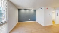 This efficiently designed studio in Phoenix, AZ offers a thoughtfully laid-out single-floor living space that maximizes every square foot. The open-concept layout seamlessly connects the kitchen and living area, creating a cohesive and functional environment.

The kitchen is well-appointed with gray shaker-style cabinetry, stainless steel appliances including a full-size refrigerator, gas range, and dishwasher, complemented by clean white quartz countertops and a classic white subway tile backsplash. A window above the sink allows natural light to filter in, brightening the workspace.

The living area features warm, light-toned hardwood flooring that extends throughout the unit, lending a sense of continuity and warmth. A standout design element is the painted brick accent wall in a deep slate-blue hue, illuminated by recessed spotlights above — offering both texture and a bold focal point. An additional white-painted brick wall provides a softer, contrasting architectural detail.

The space also includes a hallway leading to a bathroom with visible closet storage, an electrical panel, and a thermostat — reflecting practical, modern utility. Crisp white walls and clean trim throughout contribute to a bright, contemporary aesthetic that feels open and well-maintained.