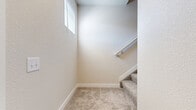 Located at 1736 Ramjet Point in Colorado Springs, Colorado, this two-story, one-bedroom, one-bathroom unit offers a well-designed layout spread across two floors. The main living level features light-toned hardwood-style flooring that flows throughout the open kitchen and living area. The kitchen is outfitted with crisp white shaker cabinets, a white tile backsplash, and a full suite of stainless steel appliances including a refrigerator with ice maker, electric range, over-the-range microwave, and dishwasher. Built-in open shelving provides additional storage and display space adjacent to the kitchen. The bathroom features warm hardwood-style flooring, a white vanity with modern hardware, and a full tub and shower combination with built-in shelving. The carpeted bedroom is a comfortable size, offering a wall-mounted mini-split HVAC unit for climate control and a window with blinds that lets in natural light. Clean white paneled doors and neutral wall tones throughout give the space a bright, move-in-ready feel. The unit also includes a dedicated utility room and closet, providing practical storage. A staircase connects the entry-level to the main living floor above.