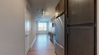 This single-floor residence offers a well-designed, open-concept layout that efficiently combines functionality with modern aesthetics. Light wood-look flooring flows consistently throughout the main living areas, creating a cohesive and clean visual throughout the space.

The galley-style kitchen is outfitted with dark wood cabinetry extending to the ceiling, providing ample storage. Stainless steel appliances include a full-size refrigerator, electric range, built-in microwave, and dishwasher. Light granite countertops contrast the darker cabinetry, and track lighting along the hallway ceiling illuminates the cooking area effectively.

The open living area adjoins the kitchen, benefiting from a large window that brings in natural light and an outdoor view. A ceiling fan is centrally positioned overhead, serving both comfort and ventilation needs.

A separate room, suitable for use as a bedroom, features a combination of wood-look and carpet flooring, along with a window fitted with blinds for adjustable light control.

The bathroom includes dark-toned cabinetry with multiple drawers, granite countertops, a framed mirror, and tile flooring. The layout is elongated, providing a practical and organized vanity area alongside the toilet and towel bar.

Overall, the space presents a clean, contemporary finish with consistent material choices throughout.