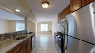 This well-appointed 2-bedroom, 2-bathroom residence is designed for comfortable, functional living across a single floor. The galley-style kitchen is a standout feature, outfitted with rich warm-toned cabinetry, granite countertops, a stainless steel appliance suite including a gas range, built-in microwave, dishwasher, and refrigerator, as well as a deep undermount sink. Decorative tile backsplash adds a refined touch to the culinary space. The kitchen flows seamlessly toward a dining area illuminated by a classic chandelier and a bright window that invites natural light into the space. Light-toned hardwood-style flooring runs through the main living and dining areas, complementing the neutral, cream-toned walls that create a clean and welcoming ambiance throughout. Tile flooring in the kitchen provides both durability and visual contrast. The open layout between the kitchen, dining, and living areas promotes an airy, connected feel that is ideal for both everyday living and entertaining. With two full bathrooms and two bedrooms, the home offers practical versatility for a variety of lifestyles. The overall design balances modern convenience with warm, inviting aesthetics.