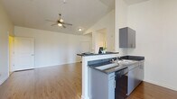 This thoughtfully designed 2-bedroom, 2-bathroom single-story residence offers a comfortable and functional layout across a well-utilized floor plan. The open-concept living and dining area is highlighted by soaring vaulted ceilings and a ceiling fan, creating an airy, spacious feel. Warm wood-look flooring flows throughout the main living spaces, complementing the bright, neutral-toned walls.

The kitchen features sleek gray cabinetry, dark granite-style countertops, stainless steel appliances including a full-size refrigerator and dishwasher, and a peninsula with bar seating that opens directly to the living area. A door with adjacent windows allows natural light to fill the kitchen and provides exterior access.

Both bathrooms are finished with hexagonal tile flooring, dark countertops, modern cabinetry, and full tub-shower combinations with curtain rods. A large vanity mirror enhances each bathroom's sense of space.

The bedrooms are carpeted for comfort, with the spacious primary bedroom offering generous square footage. The secondary bedroom includes a sliding-door closet. A dedicated laundry area and a utility space housing a water heater round out the home's practical amenities, ensuring all essential functions are neatly contained within the layout.