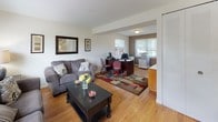This two-floor property offers a well-organized and functional layout with a warm, understated aesthetic throughout. The main level welcomes you with a bright living room featuring hardwood flooring, large windows with natural light filtering through blinds, and a front entry door with glass accents. The living area flows seamlessly into a dedicated office nook, complete with hardwood floors, a colorful area rug, and windows overlooking greenery outside. The kitchen is equipped with warm oak cabinetry, dark countertops, tile flooring, a gas range, and a double-door access point, providing both practicality and charm. Upstairs, the carpeted bedrooms offer a serene retreat. The primary bedroom is generously proportioned, featuring a classic sleigh bed frame, a dresser with mirror, and a nightstand. A second bedroom includes a large closet and multiple windows framing outdoor tree views. A versatile sitting room with plush carpet and neutral tones provides flexible living space. The bathroom is finished with white subway tile wainscoting, tile flooring, and a window for natural ventilation. Throughout, the home maintains a clean, neutral palette that creates a calm and inviting atmosphere.