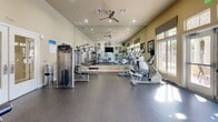 Located at 1510 Santa Diana Rd in Chula Vista, CA, this single-floor fitness center is a well-equipped community workout facility designed to support a comprehensive exercise routine. The space features a durable rubberized flooring surface that provides comfort and safety during workouts, while recessed lighting and ceiling fans ensure a well-lit and well-ventilated environment throughout.

A striking multicolored geometric accent wall in shades of teal, beige, and brown serves as a focal point, complemented by a wall-mounted flat-screen television. Full-length mirrors line one wall, enhancing the sense of space and allowing users to monitor their form during exercise. Large windows along the exterior wall invite abundant natural light, creating a bright and energizing atmosphere with views of the surrounding outdoor area.

The fitness center is outfitted with a selection of Precor brand strength machines, including cable and resistance equipment, as well as free weight benches. Cardio equipment includes multiple treadmills and elliptical trainers arranged to take advantage of the natural light from the windows. The layout is thoughtfully organized, providing ample open floor space between stations. A posted fitness center rules sign near the entrance ensures a safe and respectful environment for all users.
