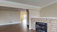 This three-floor home offers a practical and comfortable layout designed with everyday living in mind. The entry level welcomes visitors through a paneled front door with a transom window, opening into a hardwood-floored foyer that sets the tone for the rest of the home. The main living area is anchored by a striking stone-surround fireplace and flows openly into an adjacent room with access to an outdoor balcony, filling the space with natural light. The kitchen is well-equipped with dark cabinetry, granite-look countertops, stainless steel appliances including a range, microwave, and refrigerator, and durable hardwood-style flooring. Carpeted bedrooms provide comfort and warmth, with one featuring a distinctive round porthole window alongside standard windows that bring in ample daylight. Bedrooms are complemented by closets with built-in shelving. Bathrooms include a full bath with a tub-shower combination and a separate bathroom with a vanity, dark cabinetry, and wood-look flooring. Carpeted staircases with dark wood railings connect all three levels. The lower level includes a spacious attached garage with a motorized door opener and concrete flooring, offering generous storage and parking. Textured ceilings and warm neutral tones throughout create a cohesive and inviting atmosphere.