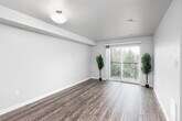This single-floor unit offers a thoughtfully designed open-concept layout that connects the kitchen and living areas seamlessly. The kitchen features warm honey-toned wood cabinetry, light granite-style countertops, hardwood-style flooring, and a full suite of appliances including a stainless steel refrigerator, black electric range, built-in microwave, and dishwasher. A half-wall peninsula separates the kitchen from the living area, providing an ideal spot for casual dining or additional prep space. The living area is bright and airy, enhanced by hardwood-style flooring and a sliding glass door that opens onto a private balcony with views of surrounding mature trees, allowing generous natural light to filter throughout the space. The bedroom features plush wall-to-wall carpeting and a window with blinds, providing a quiet and comfortable retreat. The bathroom is finished with warm wood cabinetry, a marble-style countertop vanity, a framed mirror with stylish lighting, and hardwood-style flooring, creating a clean and polished look. A hallway connects all areas efficiently, contributing to the unit's practical and comfortable flow. Overall, the space presents a neutral, modern palette with consistent finishes throughout.
