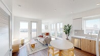 This thoughtfully designed upper-floor unit offers a clean, contemporary aesthetic defined by an all-white palette, warm wood accents, and an abundance of natural light. The open-concept living and dining area is anchored by large windows and a glass door leading to a private balcony, framing expansive city views that include palm trees and urban skyline vistas. Rich hardwood-style flooring runs throughout the main living spaces, adding warmth to the bright interior.

The kitchen is sleek and functional, featuring a two-tone design with white upper cabinetry and natural wood lower cabinets, white quartz countertops, a geometric tile backsplash, and a full suite of stainless steel appliances including a French door refrigerator, electric range, and over-the-range microwave. A dedicated workspace nook in the living area adds versatility to the layout.

The bedroom is serene and sun-filled, with a large picture window offering sweeping city and palm tree views, creating a peaceful retreat. The bathroom is finished with large-format neutral tiles in the tub/shower surround and a natural wood vanity topped with a white countertop, complemented by stone-look floor tiles. The overall ambiance is airy, modern, and light-filled throughout.