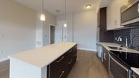 Located at 150 River's Edge Dr in Medford, MA, this single-floor residence offers a thoughtfully designed open-concept layout with contemporary finishes throughout. The kitchen is a standout feature, showcasing a full suite of stainless steel appliances, including a French door refrigerator, electric range, microwave, and dishwasher. A large center island with a white quartz countertop provides ample prep and dining space, accented by stylish pendant lighting above. Dark espresso cabinetry contrasts elegantly with white upper cabinets, while a slate-blue subway tile backsplash adds a modern touch. The kitchen flows seamlessly into a spacious living area finished with warm wood-look flooring throughout. The bedrooms are carpeted for comfort, with large windows allowing natural light and neighborhood views. Each bedroom features generous closet space, including walk-in closets with wire shelving systems. The bathrooms are finished with large-format tile flooring and dark vanities topped with white countertops. One bathroom includes a soaking tub with white subway tile surround, while a second bathroom offers accessibility features including grab bars. The overall aesthetic is clean, modern, and move-in ready.