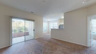 This single-story residence offers a thoughtfully designed layout that balances open living spaces with comfortable private areas. The main living and dining area is finished with warm, neutral-toned carpet and features a sliding glass door with vertical blinds that opens to an outdoor patio, allowing natural light to fill the space. A pass-through counter connects the living area to the kitchen, enhancing the open-concept feel.

The kitchen is well-equipped with stainless steel appliances, including a refrigerator, gas range, and dishwasher, all complemented by crisp white cabinetry and warm wood-toned flooring. A window above the counter provides additional natural light.

The bedrooms are generously sized, each featuring plush carpeting, neutral walls, and windows with blinds that invite natural light while maintaining privacy. The primary bedroom suite includes an en-suite bathroom with a walk-in closet area and a dedicated hallway connecting to a bathtub and vanity area.

The bathrooms are finished with tile flooring, white vanity cabinetry, single-sink countertops, and large mirrors. The overall design of the home is clean and understated, with a consistent neutral color scheme throughout that creates a bright, move-in-ready environment.