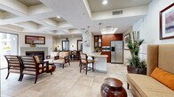 Located on Idaho Avenue in the heart of West Los Angeles, this single-floor communal space offers a thoughtfully designed open-concept layout that seamlessly connects a kitchen, dining area, and multiple living spaces. The kitchen is outfitted with rich mahogany cabinetry, granite countertops, stone-tile accent walls, and a full suite of stainless steel appliances, including a French door refrigerator, built-in microwave, and dishwasher. A peninsula with bar-height seating bridges the kitchen to the main gathering area, which features large-format tile flooring, recessed lighting, and coffered ceiling details that add architectural depth. The dining room accommodates generous seating around a substantial hardwood table, flanked by oversized framed mirrors and warm wall sconces that amplify the sense of space and light. The living room offers a comfortable, casual atmosphere with rich hardwood-style flooring, a deep sectional leather sofa, a wall-mounted television, and large windows dressed with blinds that invite natural light while maintaining privacy. Lush indoor plants are incorporated throughout, adding a vibrant, organic touch to the interior. The entrance provides a welcoming transition into the space, tying together the refined, contemporary aesthetic found throughout.