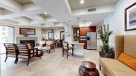Located on Idaho Avenue in the heart of West Los Angeles, this single-floor communal space offers a thoughtfully designed open-concept layout that seamlessly connects a kitchen, dining area, and multiple living spaces. The kitchen is outfitted with rich mahogany cabinetry, granite countertops, stone-tile accent walls, and a full suite of stainless steel appliances, including a French door refrigerator, built-in microwave, and dishwasher. A peninsula with bar-height seating bridges the kitchen to the main gathering area, which features large-format tile flooring, recessed lighting, and coffered ceiling details that add architectural depth. The dining room accommodates generous seating around a substantial hardwood table, flanked by oversized framed mirrors and warm wall sconces that amplify the sense of space and light. The living room offers a comfortable, casual atmosphere with rich hardwood-style flooring, a deep sectional leather sofa, a wall-mounted television, and large windows dressed with blinds that invite natural light while maintaining privacy. Lush indoor plants are incorporated throughout, adding a vibrant, organic touch to the interior. The entrance provides a welcoming transition into the space, tying together the refined, contemporary aesthetic found throughout.
