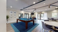 Located at 10200 Falcon Pine Blvd in Orlando, Florida, this single-story community clubhouse offers a well-appointed gathering space designed for both recreation and relaxation. The open-concept layout is anchored by a central game room showcasing a full-size billiards table set atop a vibrant blue area rug, surrounded by rich hardwood-style flooring that flows throughout the space. The ceiling features distinctive navy blue accent beams, recessed lighting, and a ceiling fan, lending the room a modern yet inviting character. Crown molding adds a refined architectural touch throughout.

Adjacent to the game room is a comfortable lounge area furnished with plush blue velvet armchairs and coordinating sofas accented with teal and navy throw pillows. Large windows dressed in sheer white curtains flood the space with natural light while offering views of the surrounding greenery and pool area.

The kitchenette is well-equipped with soft gray cabinetry, a subway tile backsplash, stainless steel appliances including a microwave and mini-fridge, a coffee station, and a spacious white-topped island with seating for multiple guests on elegant gold-framed velvet barstools. Glass partition walls connect the main lounge to a visible fitness center, providing a seamless and transparent transition between amenity spaces. Sliding glass doors open directly to the outdoor pool area, enhancing the overall sense of openness.
