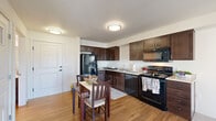 Located at 4111 133rd St SE in Mill Creek, Washington, this one-bedroom, one-bathroom residence offers a well-designed single-level layout that maximizes every square foot of its compact footprint. The open-concept kitchen, dining, and living area forms the heart of the home, creating a seamless flow ideal for everyday living. The kitchen is outfitted with rich dark espresso cabinetry, light countertops, and a full suite of black appliances including a refrigerator, range, dishwasher, and over-the-range microwave. Warm hardwood-style flooring runs throughout the kitchen and dining area, complementing the dark cabinetry for a cohesive, polished look. The living room transitions to plush carpet and features a sliding glass door that opens to a private balcony, allowing natural light to fill the space. The bedroom is a calm, neutral retreat with carpet flooring, a bright window with outdoor views, and two closets offering generous storage. The full bathroom features hardwood-style flooring, a dark wood vanity with an integrated sink, and a tub/shower combination with grab bar support. Two additional closets provide practical storage solutions throughout. The overall ambiance is clean, modern, and move-in ready.