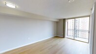 This single-floor space offers a clean, contemporary design that emphasizes simplicity and functionality. The main living area is finished with smooth light hardwood flooring that adds warmth and a sense of openness throughout the space. Neutral-toned walls provide a versatile backdrop, complemented by crisp white baseboards that give the interior a polished, well-maintained appearance. The textured ceiling adds subtle architectural character while a flush ceiling fixture provides overhead lighting.

A standout feature of this space is the floor-to-ceiling sliding glass door that opens directly onto a private balcony. Dressed with floor-length draping curtains, this transition between indoors and outdoors allows for abundant natural light to fill the interior. The balcony itself overlooks an urban cityscape, offering views of neighboring buildings and open sky — ideal for those who appreciate a connection to the surrounding environment.

The overall ambiance is airy and minimal, creating a blank canvas that is well-suited for a variety of interior styles. The combination of natural light, clean lines, and quality finishes makes this a comfortable and inviting space with strong everyday livability.