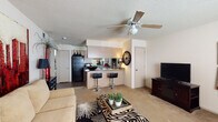 This single-story residence offers a well-organized layout that connects living, dining, and kitchen spaces in an open, functional arrangement. The living area features soft carpet flooring, a ceiling fan with light fixture, and a textured ceiling. A generously sized sofa anchors the room, complemented by a bold wall clock and decorative elements that add character to the neutral-toned walls.

The kitchen is efficiently designed with light wood cabinetry, dark countertops, and hardwood-style flooring. It is equipped with a full suite of black appliances, including a refrigerator, microwave, and dishwasher, along with a white electric range. A peninsula with bar-height seating extends toward the living area, creating a natural transition between spaces. In-unit laundry is conveniently tucked into an adjacent utility area.

Both bedrooms are carpeted and fitted with ceiling fans. Each room receives natural light through windows with blinds and offers closet storage. The full bathroom includes a tub and shower combination with sliding glass doors, a vanity with storage cabinetry, a mirror, and hardwood-style flooring, completing this practical and cohesive living space.