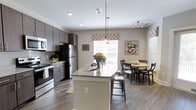 Located at 100 Underwood Dr in Summerville, South Carolina, this single-story residence offers a thoughtfully designed open-concept layout that seamlessly connects the kitchen and dining areas. The kitchen is a standout feature, boasting dark espresso cabinetry that contrasts beautifully against light-toned walls, a granite-topped center island with bar seating, and stainless steel appliances including a refrigerator and range. Recessed lighting and stylish pendant lights above the island provide ample illumination, while a track lighting system adds a modern touch. Rich wood-look flooring flows consistently throughout the space, lending warmth and cohesion to the interior. The adjacent dining area is bathed in natural light from large windows dressed with decorative valances, creating a bright and welcoming atmosphere. The overall design balances functionality with contemporary aesthetics, making the space ideal for both everyday living and entertaining. The neutral color palette, quality finishes, and open sightlines contribute to an inviting ambiance that feels both spacious and comfortable throughout.