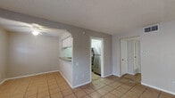 This single-story space is organized around a practical, open layout that connects the living and kitchen areas through a distinctive arched pass-through. The living room is finished with large-format ceramic tile flooring and features a ceiling fan, a textured ceiling, and a front-facing window that admits natural light. The kitchen is accessed via a separate doorway and is equipped with stainless steel appliances, including a refrigerator and electric range, white upper cabinetry, and granite-style countertops that extend along the pass-through bar, providing an additional surface for dining or food preparation.

The bedrooms are distinguished by rich, dark hardwood-style flooring, neutral-toned walls, textured ceilings, and ceiling fans. One bedroom includes a window fitted with blinds for light control. The bathroom features light ceramic tile flooring with a decorative mosaic inlay, a granite-topped vanity with white cabinetry, and a shower area clad in deep reddish-brown tile. A small window provides ventilation and a touch of natural light. Throughout the unit, clean white trim and neutral gray and beige wall tones contribute to a cohesive, understated aesthetic.