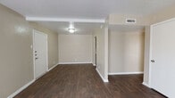 This single-floor residence offers a practical and comfortable layout with a well-defined flow between living, kitchen, and sleeping areas. The open living and dining space is finished with rich, dark hardwood-style flooring that extends throughout the main areas, complemented by neutral beige walls and crisp white baseboards. A ceiling-mounted light fixture illuminates the entry and main living area, while a set of vertical blinds covers a sliding glass door that fills the space with natural light.

The kitchen is efficiently designed with a galley-style layout, featuring dark cabinetry, granite-patterned countertops, and a full-size refrigerator. The flooring continues seamlessly from the main living area into the kitchen, maintaining a cohesive aesthetic throughout.

The bedrooms are carpeted for comfort and include ceiling fans for added ventilation. One bedroom features dual doors, offering access to a closet or an adjoining room. The bathroom is appointed with a dark wood vanity, granite-patterned countertop, an inset medicine cabinet mirror, and textured walls that add subtle visual interest.

Central HVAC vents are present throughout, ensuring climate control across the entire floor plan. The overall design is clean, neutral, and move-in ready.