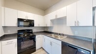 This single-level, 2-bedroom, 2-bathroom residence in Greeley, Colorado is designed with a clean, modern aesthetic and a practical layout. The kitchen is a standout feature, equipped with white shaker-style cabinetry, dark countertops, a double-basin stainless steel sink, and a full suite of black appliances including a range, over-the-range microwave, dishwasher, and refrigerator. Light wood-look flooring runs throughout the main living and kitchen areas, adding warmth and continuity to the space. A well-lit hallway connects the rooms, creating a smooth flow throughout the unit. Both bedrooms are carpeted and offer a quiet, comfortable retreat, with the primary bedroom featuring a dedicated closet with built-in rod and shelving, and direct access to one of the two bathrooms. Each bathroom is finished with white cabinetry, dark countertops, and wood-look tile flooring; one includes a tub-shower combo with built-in shelving. A notable convenience is the in-unit washer and dryer, visible from the main living area. Neutral wall tones throughout the space lend a bright, move-in-ready atmosphere well-suited for everyday living.