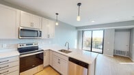 This well-appointed single-floor unit offers a thoughtfully designed open-concept layout that seamlessly connects the kitchen and living areas. The kitchen is a standout feature, showcasing crisp white shaker cabinets with matte black hardware, a classic subway tile backsplash, light quartz countertops, and a full suite of stainless steel appliances including a refrigerator, electric range, and built-in microwave. A central peninsula with an integrated sink and pendant lighting above provides both additional workspace and casual dining. Light-toned hardwood flooring runs throughout the main living area, enhancing the bright, airy atmosphere. Large windows in the living area invite generous natural light and offer views of the surrounding neighborhood. A sliding glass door leads directly to a private balcony, ideal for outdoor relaxation. The bedrooms are finished with plush carpeting, ceiling fans, and windows that continue to bring in natural light, each offering closet storage. The bathroom is finished with large-format tile flooring in a warm earthy tone, a full soaking tub with shower, a white vanity, and clean, neutral wall tones that create a calm and functional space. Throughout the unit, a consistent neutral color palette and modern finishes contribute to a cohesive, contemporary aesthetic.
