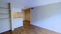 This single-floor space offers a clean and functional layout designed for comfortable everyday living. The main living area is finished with rich, dark hardwood flooring that runs throughout, adding warmth and a polished aesthetic to the interior. Neutral, light-toned walls create a bright and airy atmosphere, complemented by crisp white baseboards and trim that frame each room with a classic finish. The textured ceiling adds a subtle design detail overhead, while ceiling-mounted HVAC vents ensure year-round climate comfort throughout the space. A standout feature of the layout is the pass-through kitchen counter with a stone-style surface, which connects the kitchen to the living area — an open-concept touch that enhances the sense of spaciousness and allows for easy interaction between the two spaces. Recessed lighting in the kitchen area provides focused illumination for meal preparation. The overall design is understated and versatile, offering a neutral palette that serves as a great canvas for personalization. The practical and well-considered floor plan makes efficient use of the available space, with a layout that flows naturally from the kitchen into the living area and beyond.