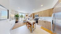Located at 208 N Federal Hwy in Pompano Beach, FL, this 3-bedroom, 2-bathroom residence offers a thoughtfully designed single-floor layout with a bright, open-concept living space. The kitchen is outfitted with warm wood-tone cabinetry, stainless steel appliances including a French door refrigerator and built-in microwave, a crisp white countertop island with bar seating, and a deep single-basin sink — all finished with large-format light tile flooring that extends throughout. Recessed lighting illuminates the space, which flows seamlessly into the living area through a sliding glass door that opens onto a generous private balcony. The balcony offers open views of the surrounding Pompano Beach skyline and lush greenery, complete with space for lounge seating under Florida's blue skies. The primary bedroom features a sliding glass door to the balcony, filling the room with natural light and outdoor views. Two additional bedrooms maintain a clean, bright aesthetic with neutral tones and tiled flooring. The bathrooms are finished with neutral stone-look tile and a glass-enclosed walk-in shower. A dedicated closet provides ample built-in storage with chrome hanging rods. The overall ambiance is coastal and contemporary, with an airy, sun-filled atmosphere throughout.