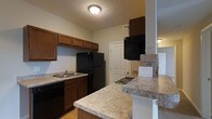 Located at 1524 Braxton Pky in Columbus, Ohio, this single-floor residence offers a practical and well-organized layout designed for comfortable everyday living. The kitchen serves as a central feature of the home, showcasing rich dark wood cabinetry that provides generous storage space both above and below the countertops. Black appliances, including a full-size refrigerator, dishwasher, and electric cooktop, lend a cohesive and modern aesthetic to the space. A double-basin sink is positioned beneath upper cabinets, maximizing workspace efficiency. The kitchen also features a peninsula-style breakfast bar with laminate countertops, creating a natural transition between the kitchen and the adjacent living area — ideal for casual dining or entertaining. Light hardwood-style flooring runs through the kitchen, adding warmth to the space. The textured ceiling and flush-mount lighting fixtures provide even illumination throughout. A closet door visible in the background suggests additional storage accessibility, contributing to the overall functionality of the floor plan. The layout flows openly, connecting the kitchen to neighboring rooms and maintaining a bright, welcoming atmosphere throughout the home.