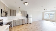 Located at 446 Waterman Ave in East Providence, Rhode Island, this 2-bedroom, 1-bathroom residence offers a thoughtfully designed single-floor layout with modern finishes throughout. Light hardwood flooring runs continuously across every room, creating a cohesive and airy feel.

The open-concept living, dining, and kitchen area forms the heart of the home. The kitchen is well-equipped with gray shaker-style cabinetry accented by gold hardware, white subway tile backsplash, light quartz countertops, and a full suite of stainless steel appliances including a range, microwave, dishwasher, and refrigerator. A stylish pendant light adds a contemporary touch above the sink area.

The two bedrooms are bright and welcoming, each featuring large windows that invite abundant natural light and offer views of the surrounding neighborhood. The rooms are finished with neutral wall tones that complement the warm wood floors.

The bathroom is clean and functional, featuring a full tub-shower combination, a gray vanity with a white sink, and a well-lit mirror. Additional utility is provided by a dedicated laundry room and a utility space. The overall design is modern, clean, and move-in ready, making this an efficient and comfortable residence in East Providence.