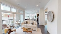 This single-floor residence features a thoughtfully designed open-concept layout that seamlessly connects the living, dining, and kitchen areas. Dark hardwood flooring runs throughout the main living spaces, complementing the bright white walls and recessed lighting overhead. The living room is anchored by large floor-to-ceiling windows and sliding glass doors that open onto a private balcony, flooding the space with natural light and offering views of the surrounding urban environment.

The kitchen is well-appointed with dark wood cabinetry, a white quartz waterfall island with an undermount sink, stainless steel appliances including a refrigerator, electric range, and built-in microwave, and a subway tile backsplash. Pendant lights above the island and a bank of large windows in the adjacent dining area enhance the bright, airy atmosphere.

The two bedrooms feature plush carpeting, ceiling fans, and generously sized windows with blinds and sheer curtains. Each room offers comfortable proportions with ample natural light. The unit includes two bathrooms: one with a glass-enclosed walk-in shower and dark hardwood floors, and a second featuring a soaking tub-shower combination with white tile surround and a wood-toned vanity with quartz countertops.