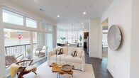This single-floor residence features a thoughtfully designed open-concept layout that seamlessly connects the living, dining, and kitchen areas. Dark hardwood flooring runs throughout the main living spaces, complementing the bright white walls and recessed lighting overhead. The living room is anchored by large floor-to-ceiling windows and sliding glass doors that open onto a private balcony, flooding the space with natural light and offering views of the surrounding urban environment.

The kitchen is well-appointed with dark wood cabinetry, a white quartz waterfall island with an undermount sink, stainless steel appliances including a refrigerator, electric range, and built-in microwave, and a subway tile backsplash. Pendant lights above the island and a bank of large windows in the adjacent dining area enhance the bright, airy atmosphere.

The two bedrooms feature plush carpeting, ceiling fans, and generously sized windows with blinds and sheer curtains. Each room offers comfortable proportions with ample natural light. The unit includes two bathrooms: one with a glass-enclosed walk-in shower and dark hardwood floors, and a second featuring a soaking tub-shower combination with white tile surround and a wood-toned vanity with quartz countertops.