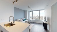 Located in Chicago's prestigious Gold Coast neighborhood, this modern high-rise residence at 1201 N LaSalle Drive offers a well-appointed single-floor layout with sleek contemporary design throughout. The open-concept living area is a standout feature, anchored by expansive floor-to-ceiling windows that frame sweeping views of the Chicago skyline, filling the space with abundant natural light. Wood-plank flooring runs throughout, complementing the cool gray palette of the walls and modern track lighting overhead. The kitchen is outfitted with white cabinetry, light quartz countertops, and stainless steel appliances, including a French-door refrigerator and dishwasher, offering both style and functionality. The primary bedroom enjoys direct access to a balcony with city views, creating a serene retreat. A secondary bedroom provides a clean, minimalist space with crisp white walls and wood flooring. The primary bathroom is elegantly finished with large-format marble-style tile, a dual-sink vanity with warm wood cabinetry, a backlit mirror, and a glass-enclosed walk-in shower. A second full bathroom mirrors the same refined aesthetic with marble tile flooring and a matching wood vanity. This residence delivers a polished urban living experience in one of Chicago's most sought-after locations.