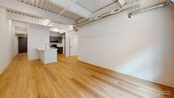 Located in the heart of Lancaster, PA, this thoughtfully designed unit at 101 N Queen St blends modern finishes with industrial character. The open-concept living and kitchen area serves as the centerpiece of the space, featuring light hardwood flooring, exposed structural beams, and ductwork along the soaring ceiling that add an urban loft aesthetic. The kitchen is equipped with dark cabinetry, stainless steel appliances, and a white island with a sink, creating a functional and stylish hub for daily living.

Two carpeted bedrooms offer a comfortable contrast to the hardwood common areas. Each bedroom benefits from the elevated ceilings and exposed mechanical elements consistent throughout the unit. One bedroom includes a built-in closet with shelving, while windows throughout frame views of the surrounding historic brick architecture, filling the space with natural light.

The full bathroom is well-appointed with a dark wood vanity, white countertop, tile flooring, and a glass-enclosed walk-in shower with tile surround. A secondary half-bath provides added convenience. A connecting hallway with a utility panel ties the layout together efficiently. Clean white walls and contemporary finishes throughout create a bright, cohesive living environment in this vibrant downtown Lancaster location.