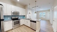 Located at 711 Beach Blvd in Jacksonville Beach, Florida, this well-designed one-bedroom, one-bathroom residence offers a efficient and thoughtfully laid-out single-floor plan. The open-concept kitchen and living area serves as the heart of the home, featuring crisp white shaker cabinetry, a teal tile backsplash, granite countertops, and a full suite of stainless steel appliances including a range, microwave, and dishwasher. A peninsula island with an undermount sink and pendant lighting doubles as a casual dining or workspace. Light wood-style flooring runs throughout the main living areas, complementing the neutral warm-toned walls and creating a clean, airy aesthetic. The living area is brightened by a large window and a glass-panel entry door with a transom window above, allowing natural light to pour in. Views of the outdoor pool area are visible from the living space windows, adding a resort-like quality. The carpeted bedroom is a comfortable retreat, equipped with a ceiling fan, ample natural light from multiple windows, and access to a walk-in closet with wire shelving. The full bathroom features granite counters, white cabinetry, and a tiled tub/shower combination. Track and pendant lighting throughout add a modern, polished finishing touch.
